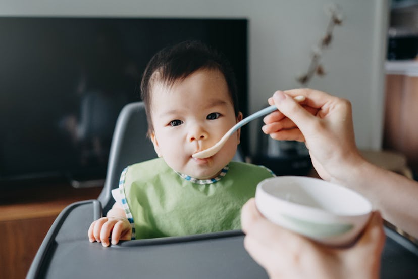 A baby eating pureed food while sitting in a high chair 