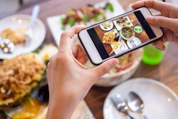 A woman holding her phone over a table full of food and taking a photo of the Thanksgiving dinner.