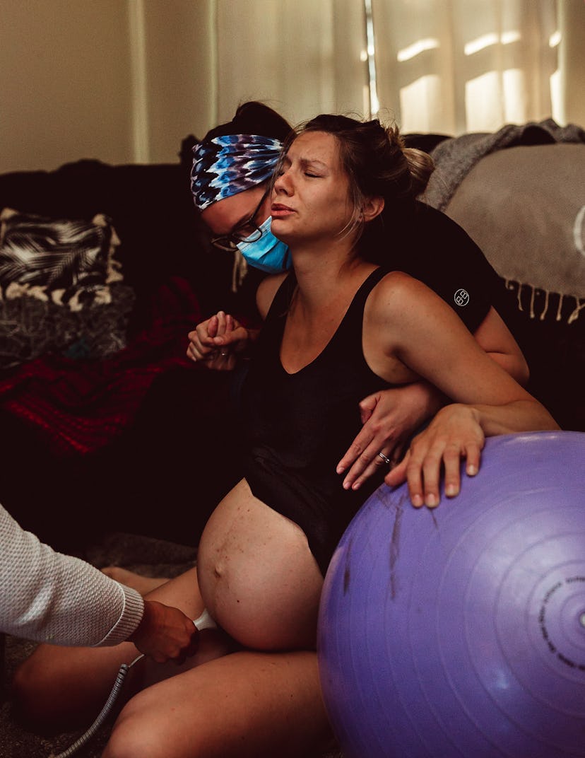 mother labors with purple birthing ball as doula and midwife support