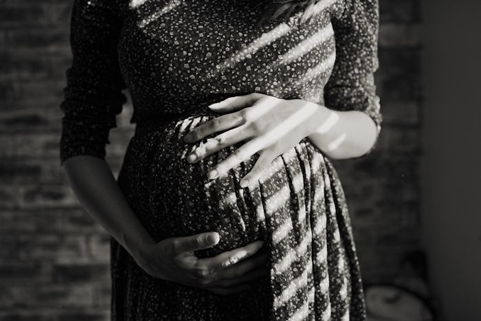 Pregnant woman in patterned dress, holding midsection