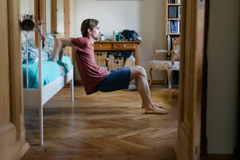 A young man using his bed to do body weight exercises at home to keep fit.