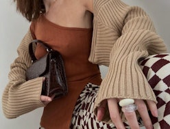 A woman in a holiday outfit; brown off-the-shoulder top, beige sweater, black-white checked pants, a...