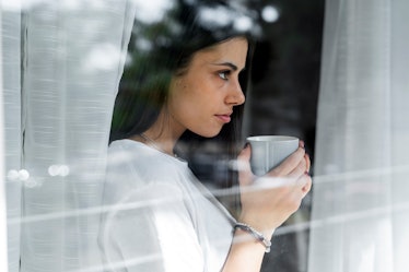 Young woman with cup of coffee behind windowpane