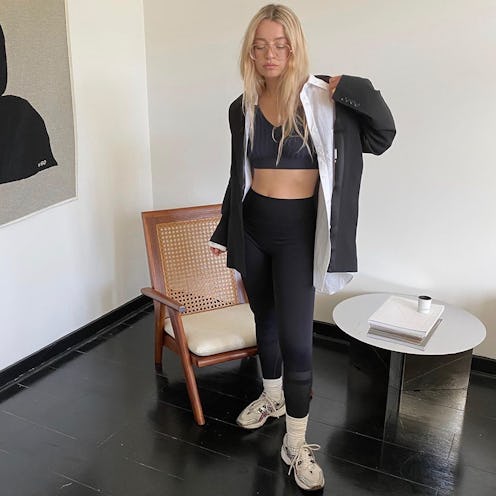 A woman wearing black leggings with a black top, white shirt, an oversized blazer and beige sneakers