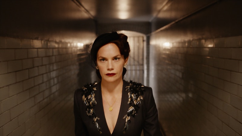 Mrs Coulter (Ruth Wilson) wearing a black jacket and hat and walking along a tiled corridor