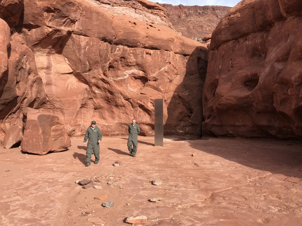 Two men approach the monolith.