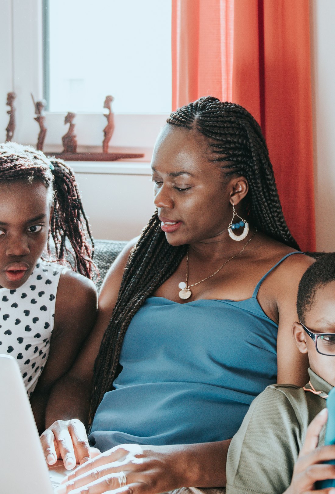 A Black mom works on a laptop; her two children sit on either side of her.