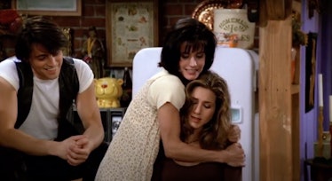 Monica hugs Rachel who is sitting at the table in the kitchen on 'Friends.'