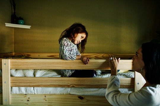 A little girl is sitting in her top bunk bed, looking at her mom.