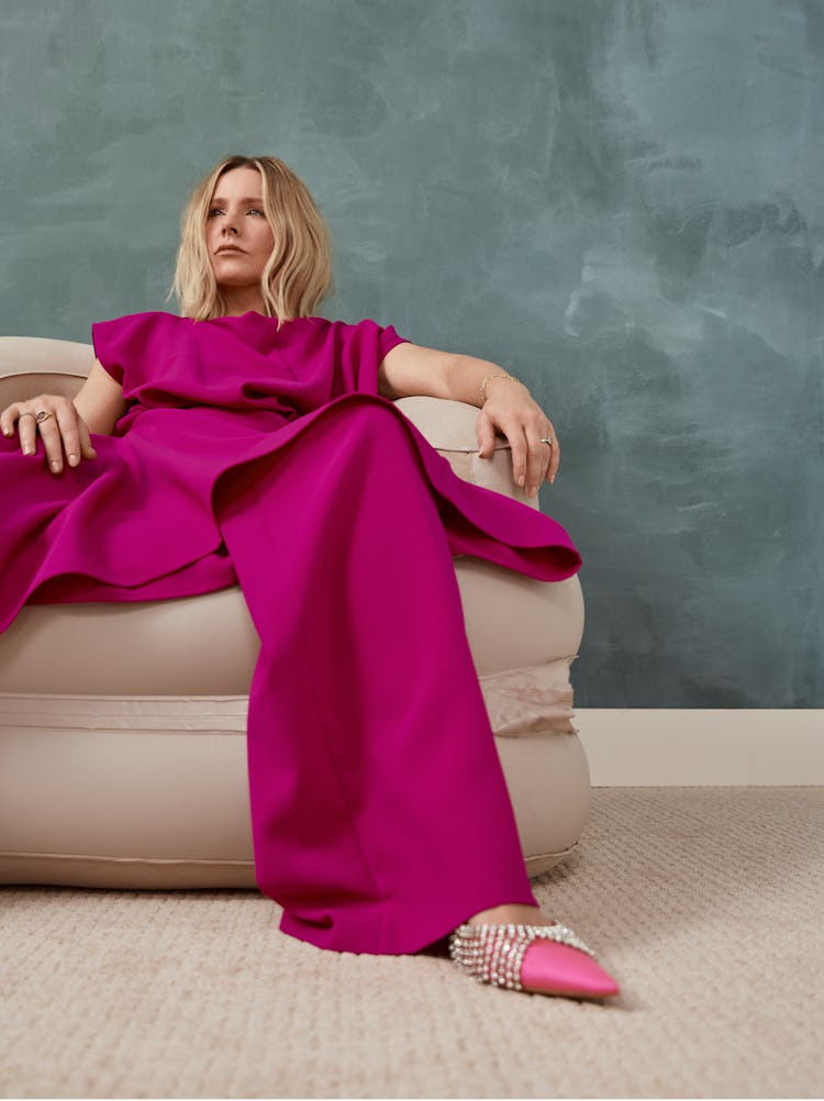 Kristen Bell posing in a beige armchair in a magenta Christopher John Rogers top and pants and studd...