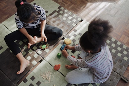 Two little girls are seen from above, playing with playdo or putty on a woven mat.
