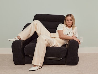 Kristen Bell lying in an armchair in a beige Dior vest, top, and pants, white Reike Nen shoes and a ...