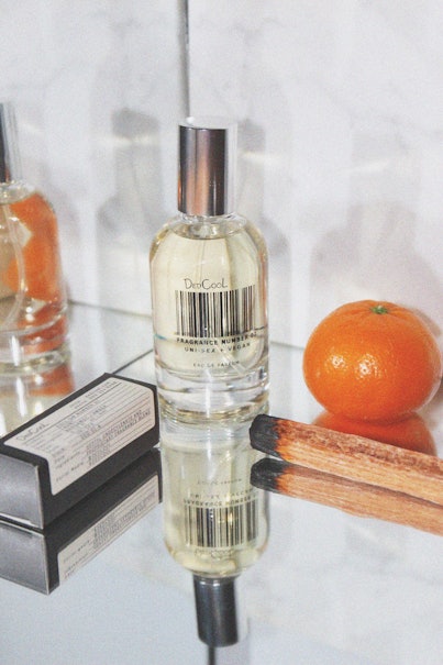 A single tangerine and DedCool perfume placed on an inclined glass table.