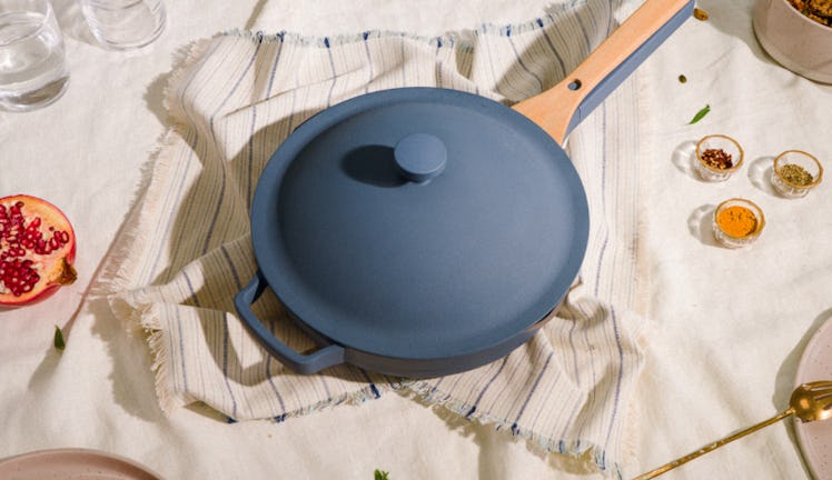 The blue salt Always Pan from Our Place sits on a dining room table with a kitchen towel underneath....