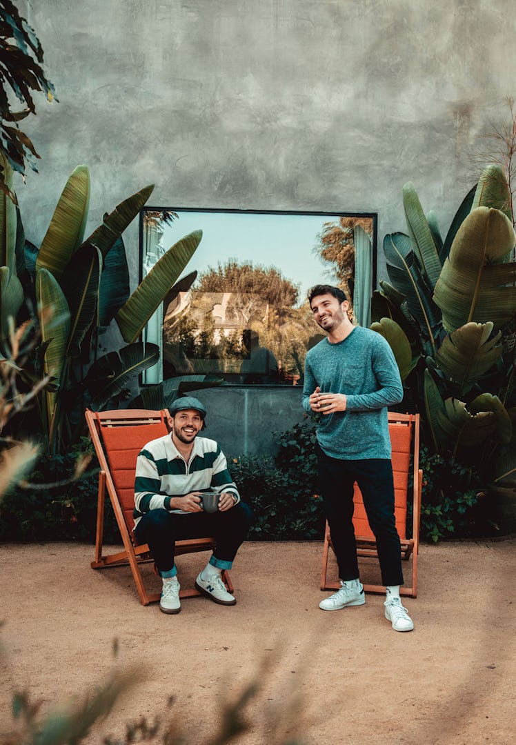 Vlog Squad's Zane Hijazi and Heath Hussar laugh while sitting and standing in front of greenery outd...