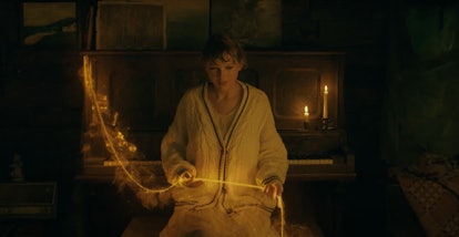 Taylor Swift holds a gold strand in her hands while sitting at a piano bench and wearing a cardigan ...