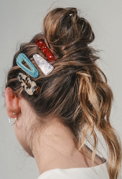 The back of a woman's head with a messy bun and different patterned clips on the side 