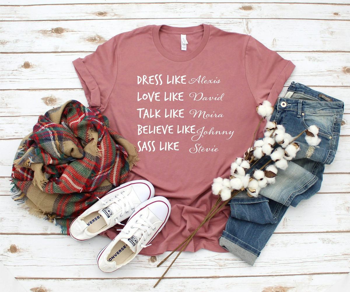A 'Schitt's Creek" inspired tee sits on the floor with converse sneakers and jeans.