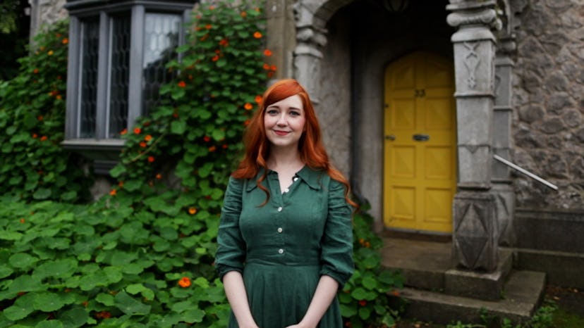 Rebecca Stice posing in a green dress in front of her tiny Irish gatehouse