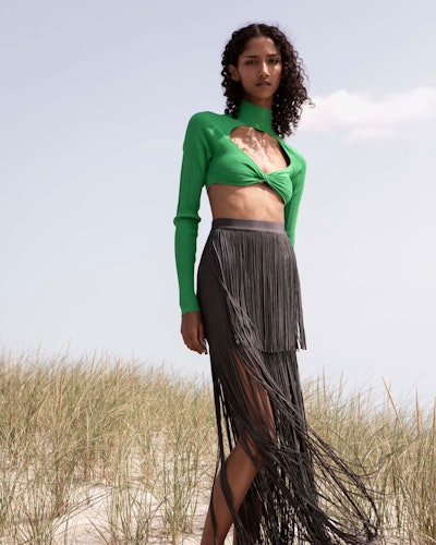 A model posing in a green cut-out crop top and a black fringe maxi skirt by Herve Leger