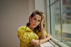 A brunette woman in a yellow-green polka-dot dress with puff-sleeves leaning near a window