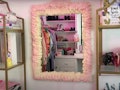 A DIY pink foam mirror sits on the wall next to filled shelves. 