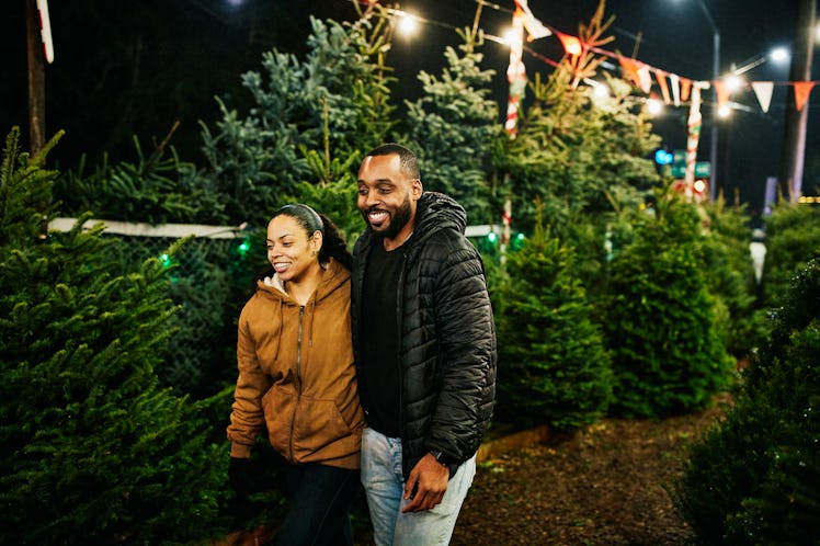 Smiling couple walking through Christmas tree lot while shopping for tree