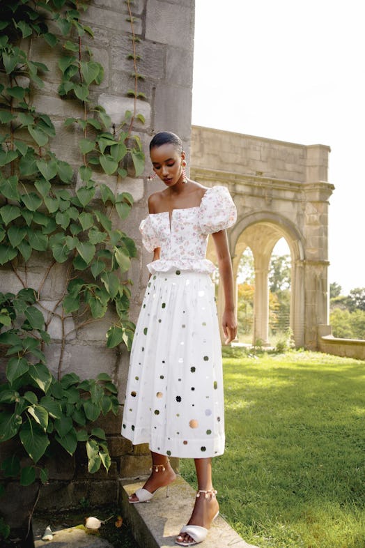 A model wearing a white midi skirt embellished with golden polka dots, paired with a flower-patterne...