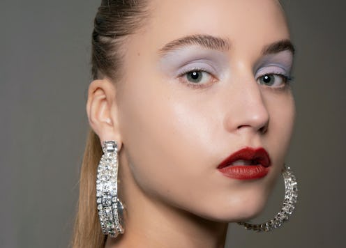 A model with a high ponytail, large hoop earrings, red lipstick and light blue eyeshadow