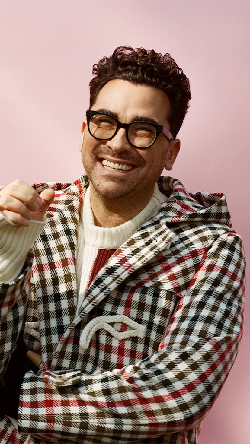 Dan Levy in a plaid jacket and a white sweater smiling