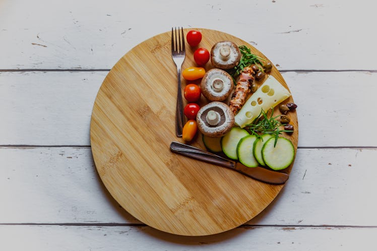 A cutting board in the shape of a clock with a fork and knife as hands and food filling one section