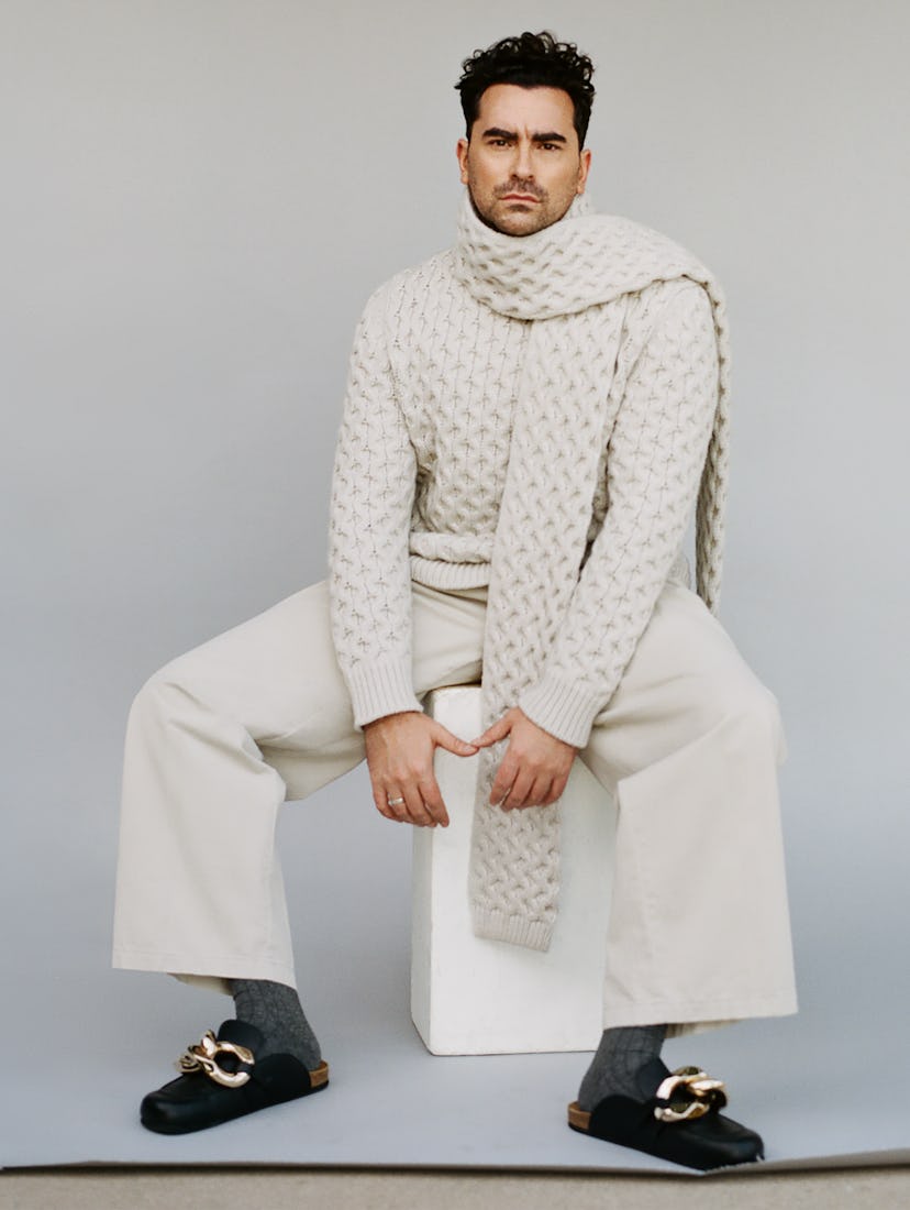 Dan Levy in a white Canali sweater and scarf, grey Tie Bar socks, black JW Anderson shoes and white ...