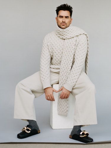 Dan Levy in a white Canali sweater and scarf, grey Tie Bar socks, black JW Anderson shoes and white ...
