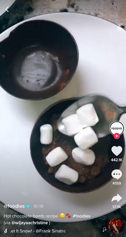 Someone spoons some hot cocoa mix into a homemade hot chocolate bomb. 