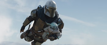A character in armor carrying Baby Yoda and flying through the sky