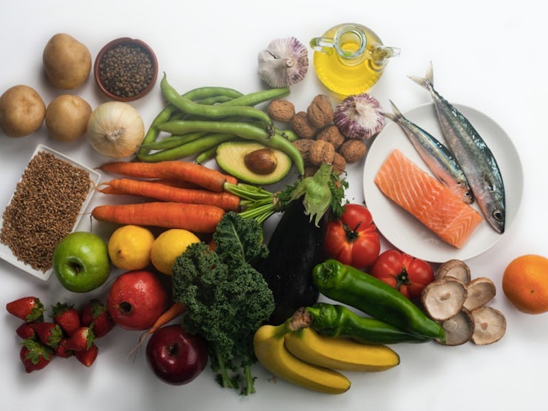 Olive oil, avocado, garlic, onion, potatoes, carrots, bananas, apples, strawberries, and fish on a w...
