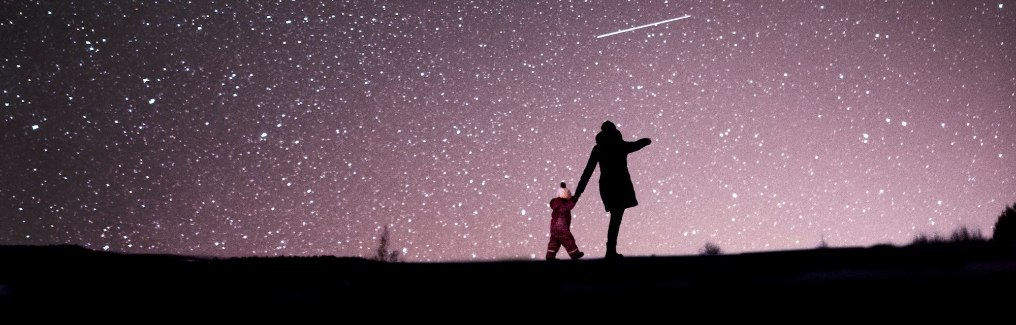 A mother and child in a dark field, seen from afar, under a glorious night sky filled with stars.