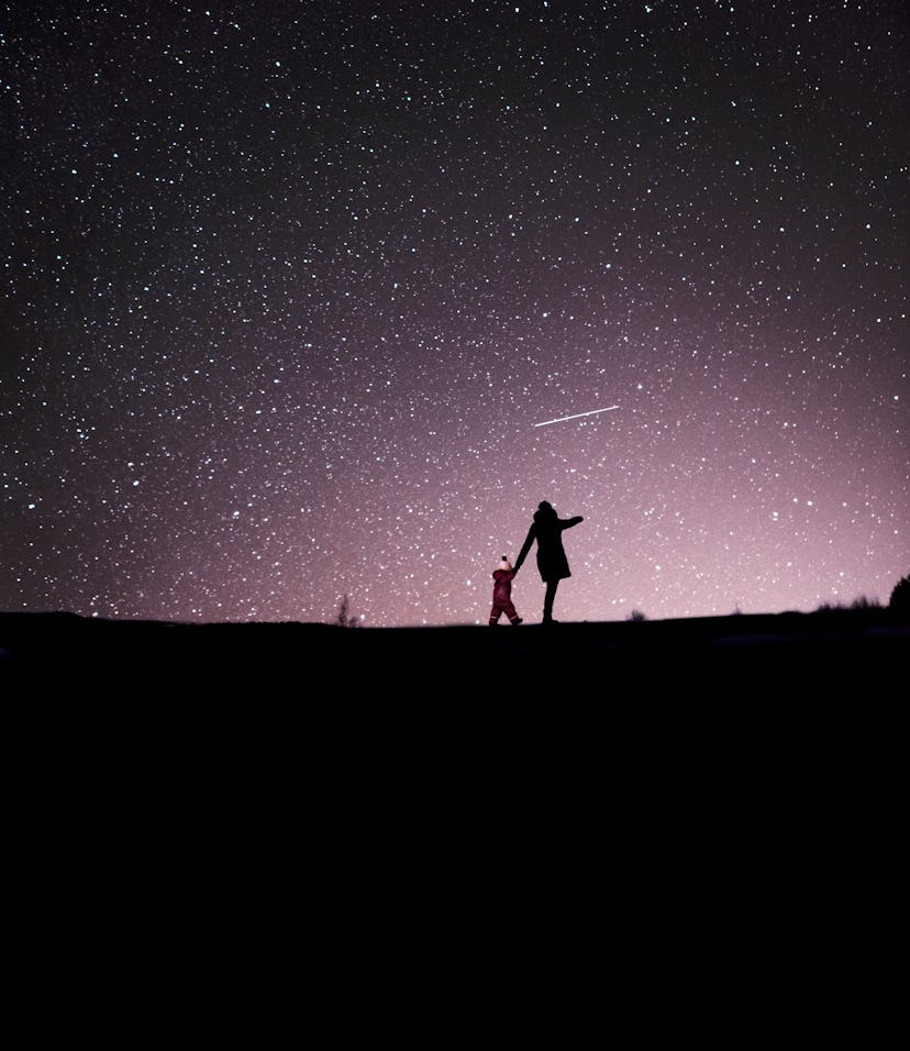 A mother and child in a dark field, seen from afar, under a glorious night sky filled with stars.