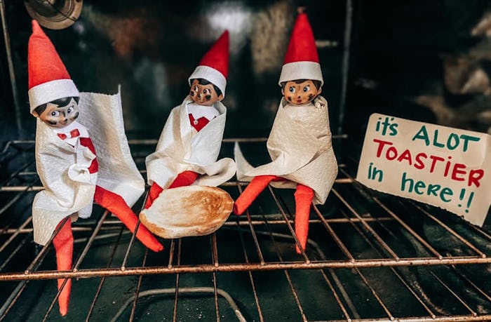 Three Elf on the Shelf elves sit wrapped in blankets in an oven around a toasted bun with a sign tha...