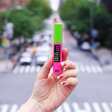 A woman's hand holding a bottle of Maybelline Great Lash with a busy street in the background