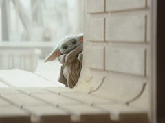 Baby Yoda from Disney's 'The Mandalorian' peaks around a concrete wall.
