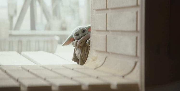 Baby Yoda from Disney's 'The Mandalorian' peaks around a concrete wall.