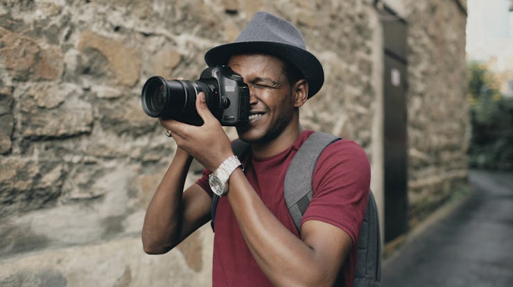 A man in a red shirt and a hat holding a dslr camera up to his eye