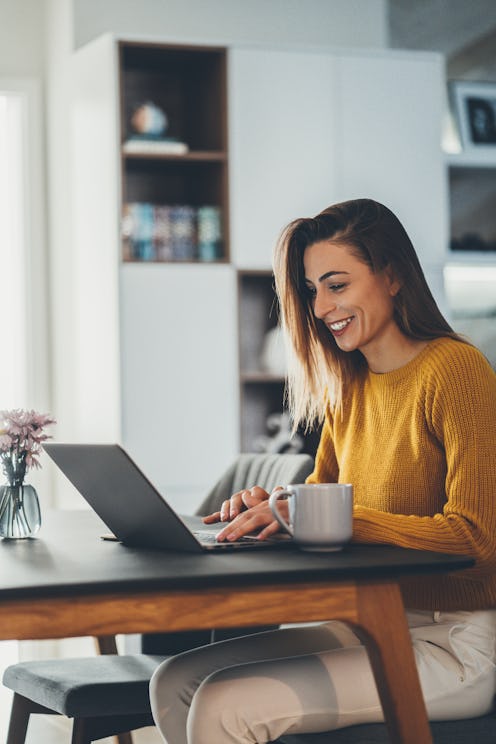 A woman at her laptop with coffe on the table having her work from home morning routine