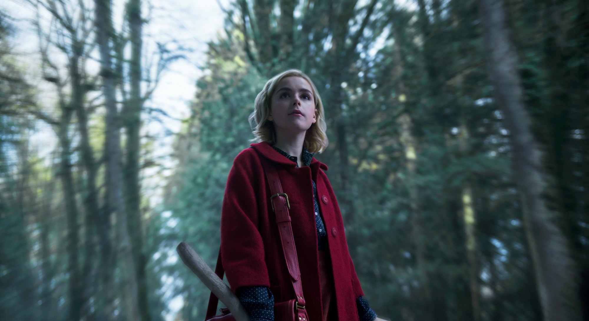 A still of Kiernan Shipka, from Chilling Adventures of Sabrina, standing in a wooded area, wearing a...