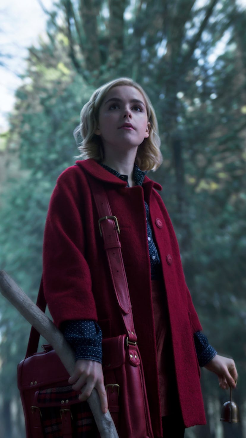 A still of Kiernan Shipka, from Chilling Adventures of Sabrina, standing in a wooded area, wearing a...