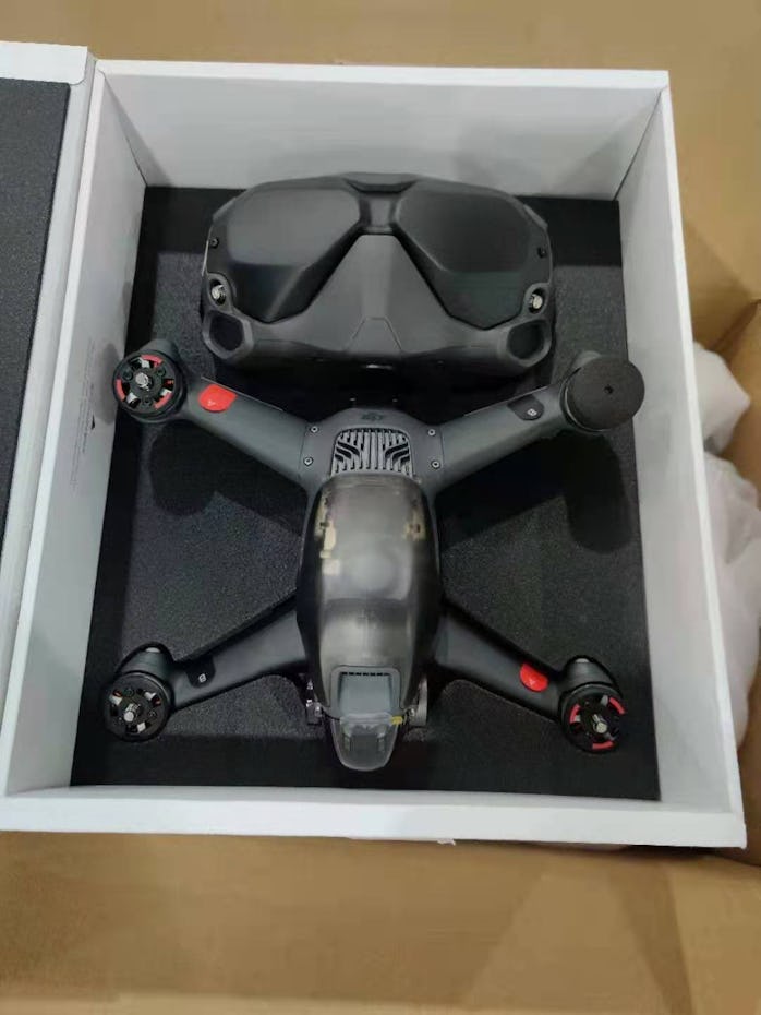 A possible DJI FPV drone in a white box. The body of the drone is mostly black and gray with a dulle...