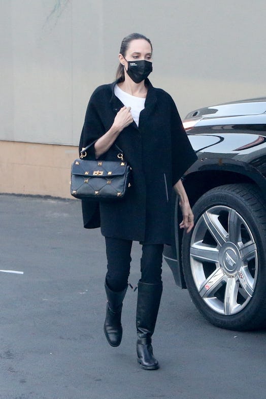 Angelina Jolie walking in a black cape coat and black skinny jeans