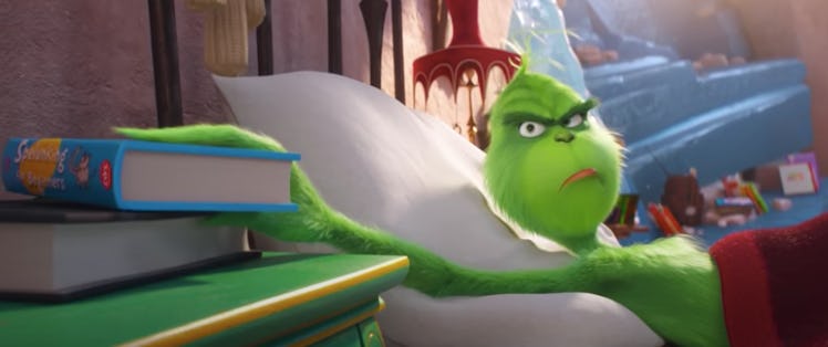 The Grinch frowns while grabbing a book in bed.