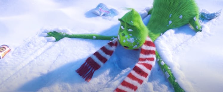 The Grinch lays on his stomach in the snow after getting knocked over by an inflatable snowman.